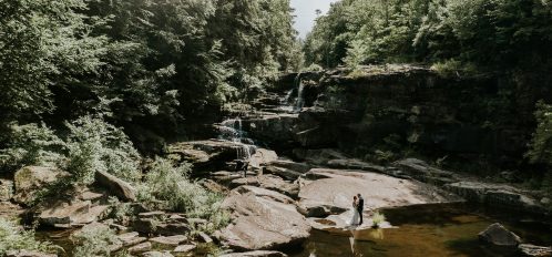 wedding couple stand before vast waterfall